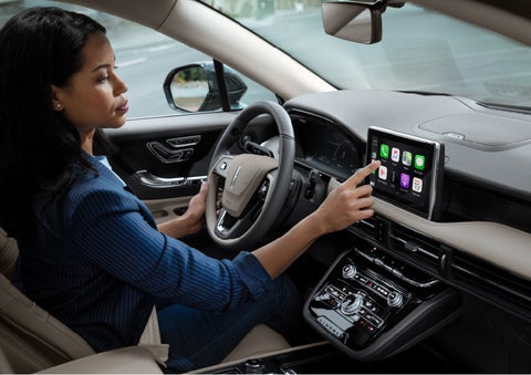 A woman in the driver's seat of a 2022 Lincoln Corsair is touching the center digital screen to connect to Apple CarPlay® | Sentry Lincoln in Medford MA