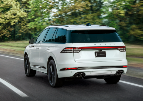 A white 2025 Lincoln Aviator® SUV is being driven away down a road lined with colorful trees. | Sentry Lincoln in Medford MA