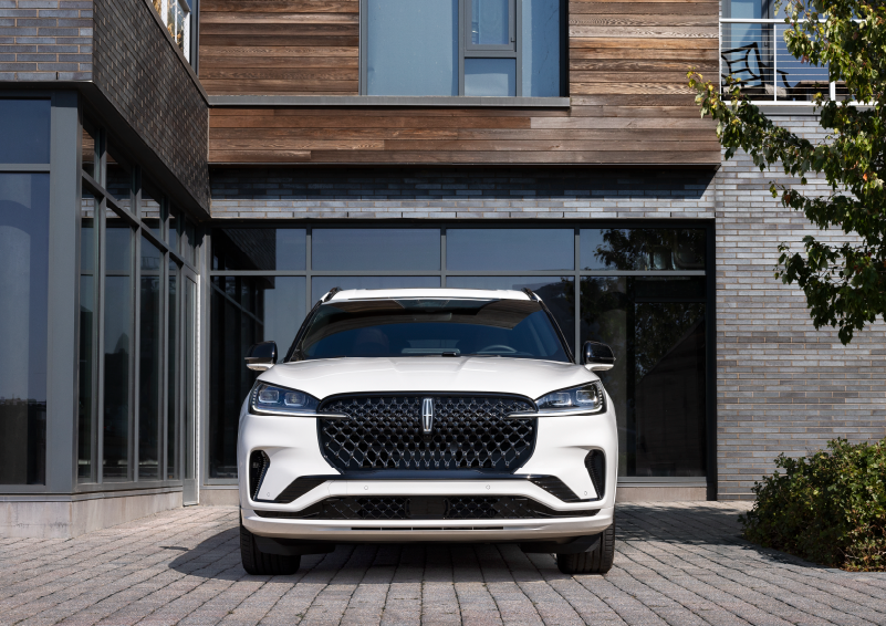 A white 2025 Lincoln Aviator® SUV is shown parked outside a modern building with gray brick and wood accents. | Sentry Lincoln in Medford MA