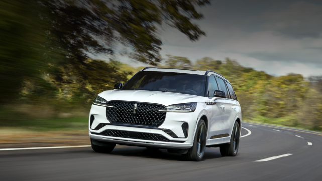 A white 2025 Lincoln Aviator® SUV is being driven down a road lined with trees. | Sentry Lincoln in Medford MA