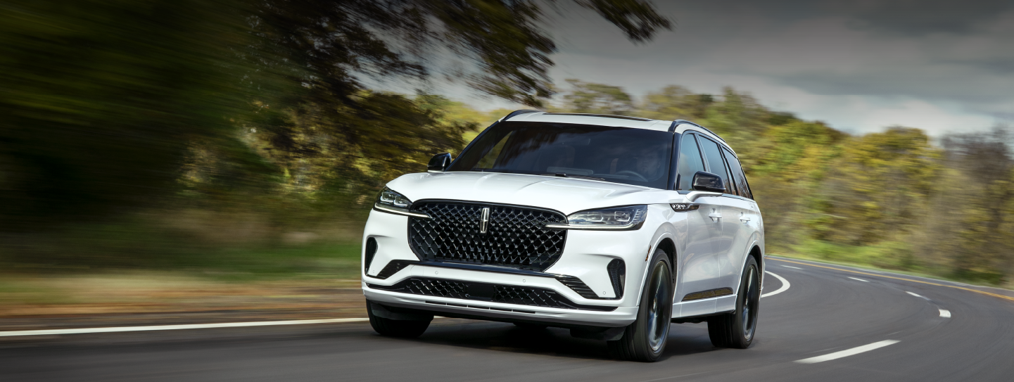 A white 2025 Lincoln Aviator® SUV is being driven down a road lined with trees. | Sentry Lincoln in Medford MA