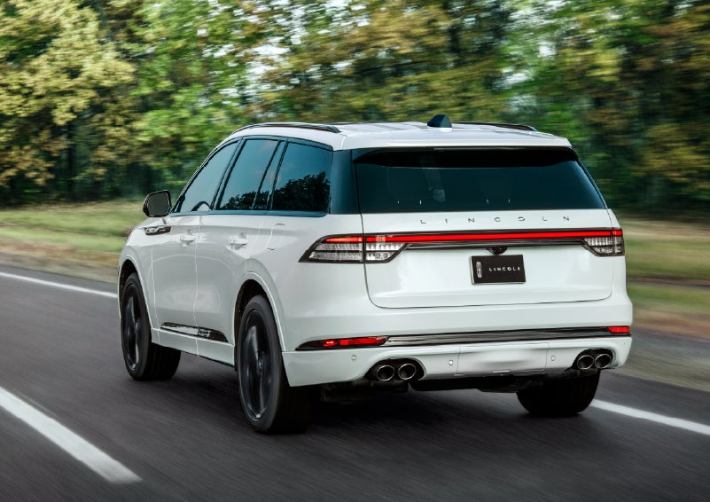 A white 2026 Lincoln Aviator® SUV is being driven away down a road lined with colorful trees. | Sentry Lincoln in Medford MA