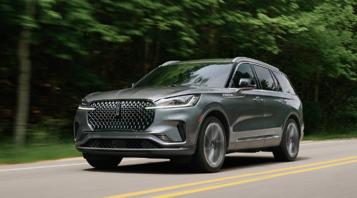 A 2027 Lincoln Aviator® SUV is being driven down a road lined with trees. | Sentry Lincoln in Medford MA